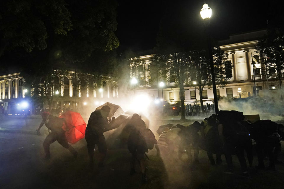 Protesters take cover from tear gas fired by police outside the Kenosha County Courthouse, late Monday, Aug. 24, 2020, in Kenosha, Wis. (AP Photo/David Goldman)