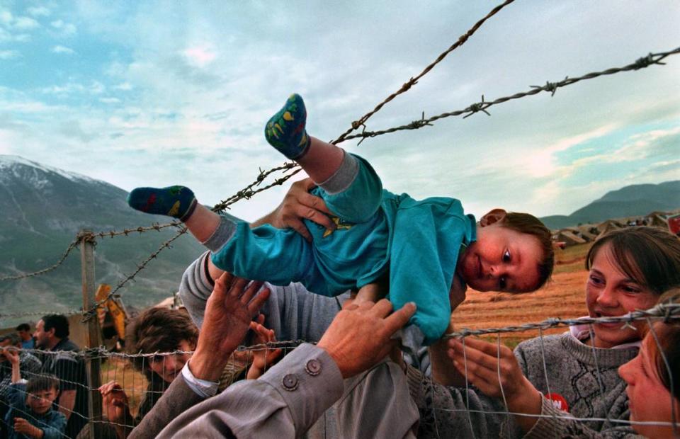 This 1999 photograph by Carol Guzy of the Washington Post is included in the “W|ALLS” exhibit. Uptown. Titled “Life in Exile: The camps,” it shows 2-year-old Agim Shala being passed through a barbed wire fence at the Arab camp in Kukes, Albania to be reunited with family members who fled Kosovo.