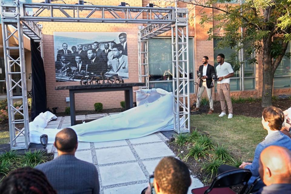 Andrew Berry, left rear, general manager of the Cleveland Browns, and Donovan Mitchell, right, Cleveland Cavaliers guard, unveil a sculpture commemorating the 1967 Cleveland summit with Muhammad Ali, Jim Brown and others, Wednesday, Oct. 11, 2023, in Cleveland. The sculpture is a representation of the press conference table where the Black athletes sat, with a photo of the event at rear. (AP Photo/Sue Ogrocki)