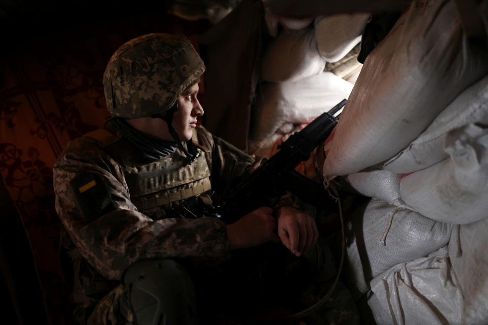 A Ukrainian soldier looks out from a small opening in a sandbag barricade at a checkpoint. 