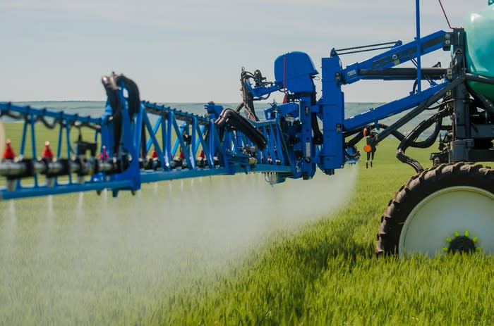 Blue tractor in a green field with crop spraying attachment on back.