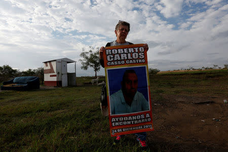 Rosalia Castro holds a poster with a picture of her missing son, Roberto Casso, as she stands by the gate to a plot of land where skulls were found at unmarked graves, on the outskirts of of Veracruz, Mexico March 16, 2017. The poster reads: "Help us find him. December 24, 2011." REUTERS/Carlos Jasso