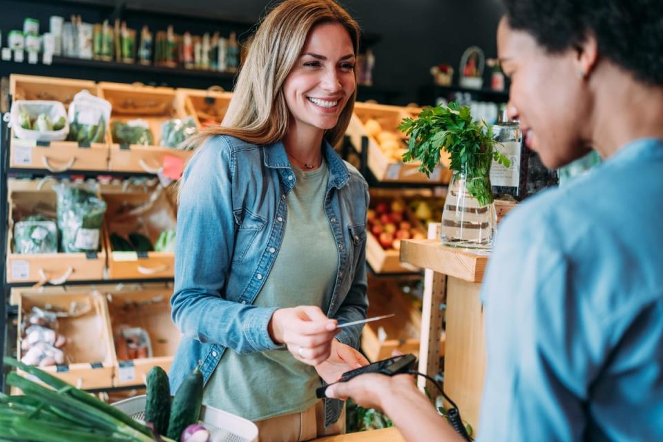 Two people smile while processing a transaction in a store using a credit/debit card reader. 