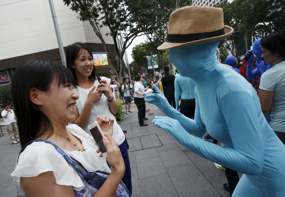 Japanese passer-bys are greeted by a participant wearing Zentai costume in a march down the shopping district of Orchard Road during Zentai Art Festival in Singapore