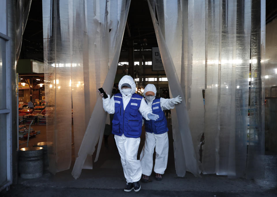 Workers wearing protective suits walk before they spray disinfectant as a precaution against the COVID-19 at a market in Seoul, South Korea, Thursday, Feb. 27, 2020. The new illness persists in the worst-hit areas and spreads beyond borders. (AP Photo/Lee Jin-man)