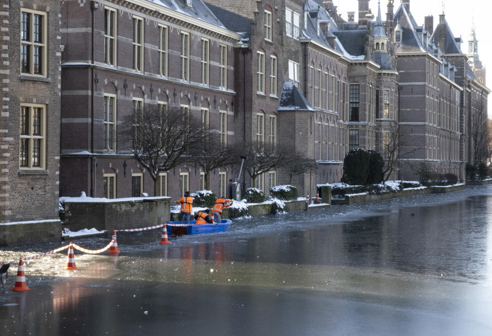 Three men in a boat hacked away at ice to create a watery perimeter around the Dutch prime minister's office in The Hague, Netherlands, Thursday, Feb. 11, 2021. With ice likely thick enough in coming days for people to skate on the Hofvijver lake that fringes one side of the Dutch parliamentary complex, workers made sure the skaters couldn't get right up to Prime Minister Mark Rutte's office by bashing through ice. (AP Photo/Mike Corder)