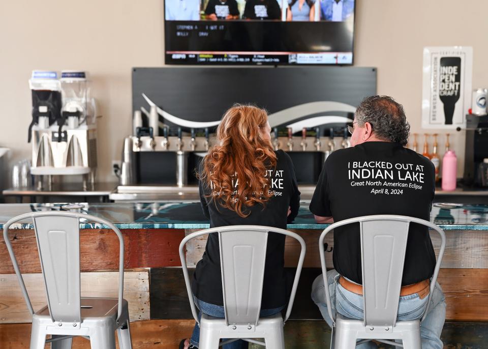 Lura Easton and Tony Searfoss sit at the bar of Indian Lake Brewing Company on April 8, 2024, for a total solar eclipse party. The Indian Lake residents bought their "I Blacked Out at Indian Lake" t-shirts from a local retailer to support the community following a deadly tornado that tore through the area in February.