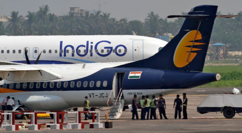 Airport staff stand next to parked passenger jets of IndiGo and Jet Airways at an airport in Kolkata