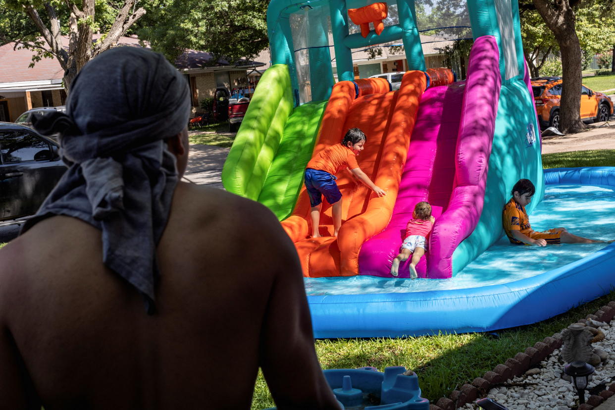 Issac Montelongo watches neighborhood kids play in the water during a heatwave with expected temperatures of 102 F (39 C) in Dallas, Texas, U.S. June 12, 2022. Though the heat wave caused electricity use in Texas to reach an all time high, the power grid remained largely stable without major issues.    REUTERS/Shelby Tauber