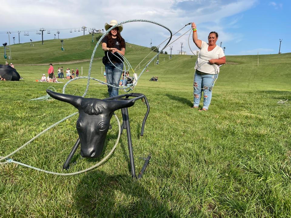From left, Taylor Tuttle, a Howell Western Wear employee, shows Natalie Winans how to throw a lasso at the Yellowstone Country Music Festival at Mt. Brighton on Saturday, July 22, 2023.