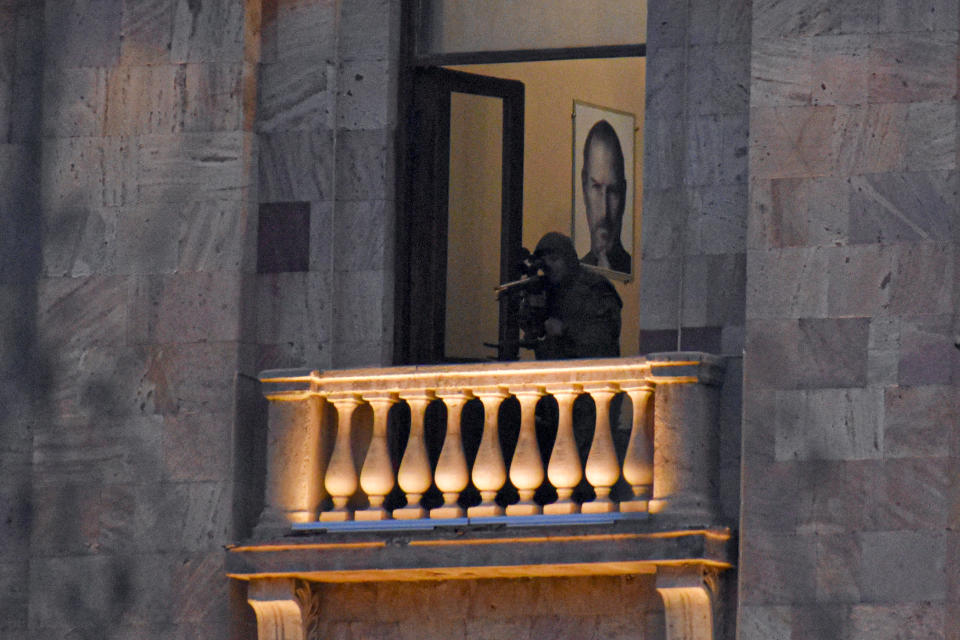 A security agent points a sniper rifle from a window of the Parliament building with a portrait of former Apple Chairman and CEO Steve Jobs on the wall as opposition demonstrators rally to pressure Armenian Prime Minister Nikol Pashinyan to resign in Yerevan, Armenia, Wednesday, March 3, 2021. Armenia’s prime minister has scored a point in his spat with the top military brass, advancing his motion to fire the country’s top military officer. A political crisis sparked by Armenia’s defeat in the conflict with Azerbaijan over the Nagorno-Karabakh region escalated last week when the military’s General Staff demanded the resignation of Prime Minister Nikol Pashinyan following his move to dismiss a top general. (Hrant Khachatryan/PAN Photo via AP)