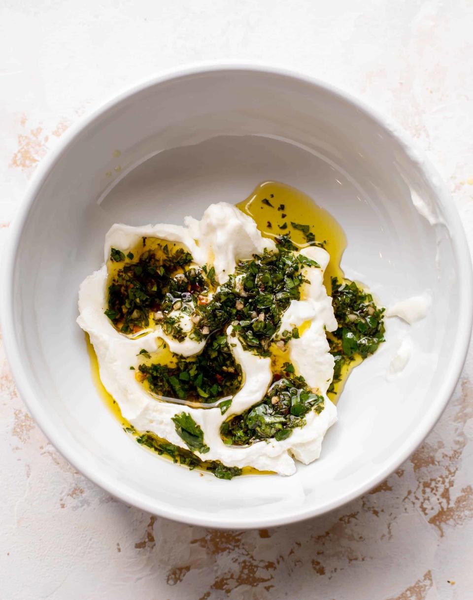 A bowl of whipped feta cheese topped with herbs, olive oil, and spices