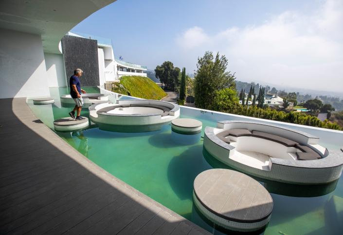 a man walks on circular structures in a blue-green pool at mansion The One Bel Air