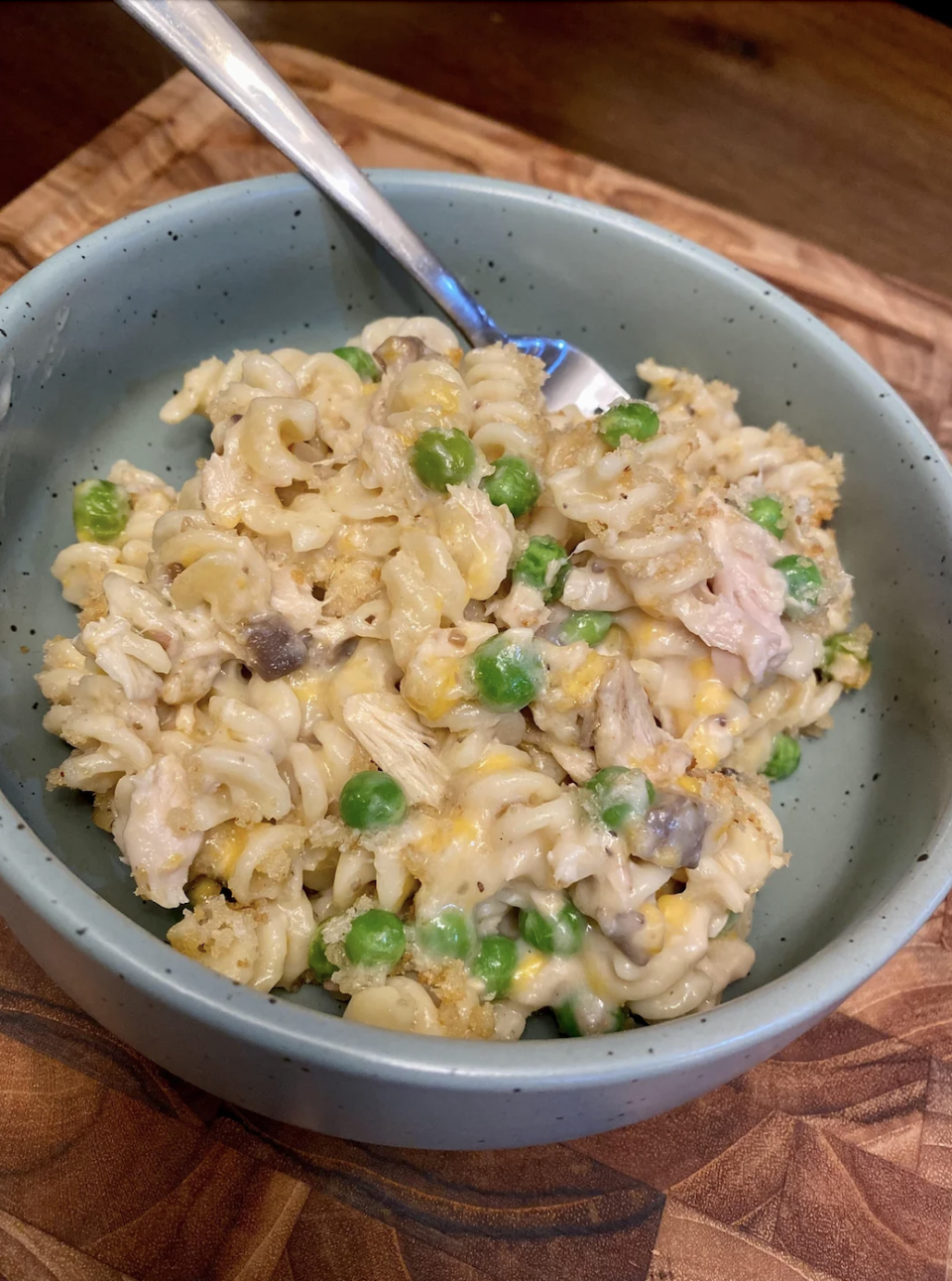 A bowl of creamy pasta with peas, mushrooms, and shredded chicken, with a fork resting in the bowl