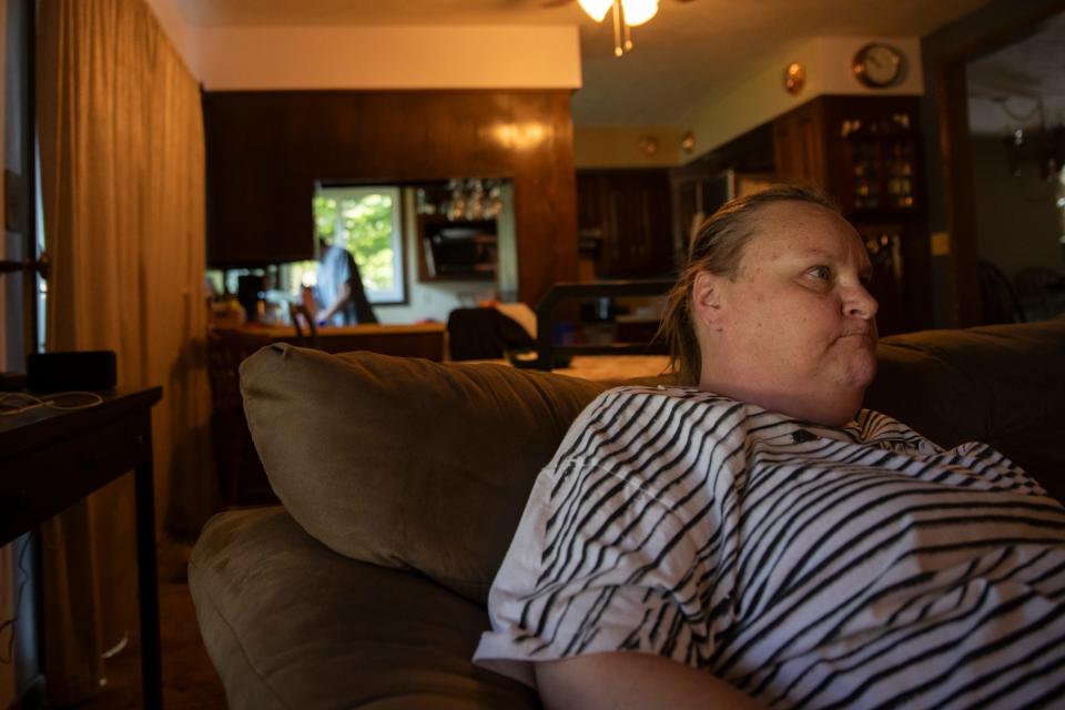 Melissa McDonald sits in the home of Craig Coburn-McDonald, watching a movie, as Craig cleans off tools he was using to disassemble her bed frame after she moved out of Portage Manor, on July 31, 2023. 