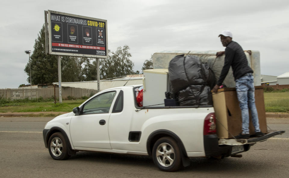A man standing in the back of a utility van drives past a billboard explaining coronavirus in Vosloorus, east of Johannesburg, South Africa, Thursday, April 2, 2020. South Africa went into a nationwide lockdown for 21 days in an effort to mitigate the spread to the coronavirus. The new coronavirus causes mild or moderate symptoms for most people, but for some, especially older adults and people with existing health problems, it can cause more severe illness or death. (AP Photo/Themba Hadebe)