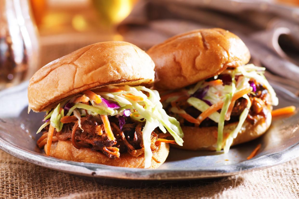 5-ingredient slow-cooker pulled pork in two burgers on a stainless steel plate with a blurred background of tableware