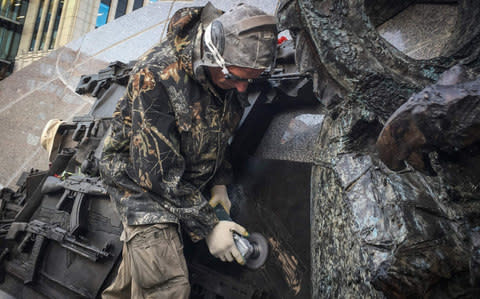 A man uses an angle grinder as he removes a sketch allegedly featuring German StG44 rifle - Credit: Mladen Antonov/AFP