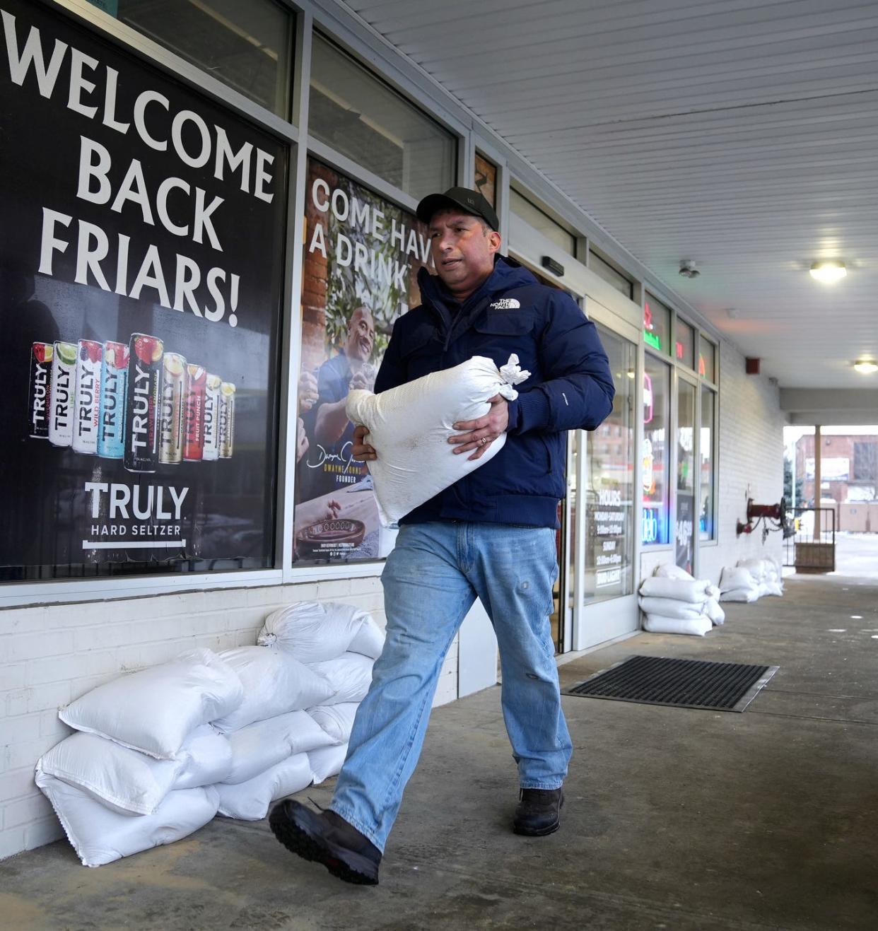 Walter Lemus, owner of First Point Sweeping and Maintenance, carries one of the many sand bags, he and his employees, were putting around doors of businesses at the Wanskuck Plaza on Branch Avenue in Providence on Tuesday afternoon in preparation for incoming heavy rain. The plaza flooded during heavy rain in September.