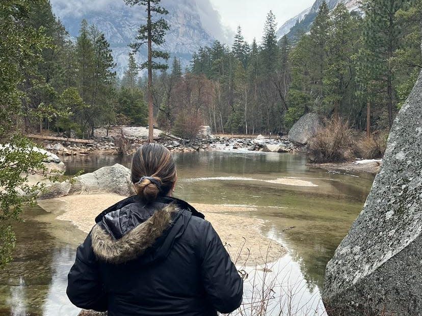 Danielle, standing at a small body of water, looking out at the trees and mountains.