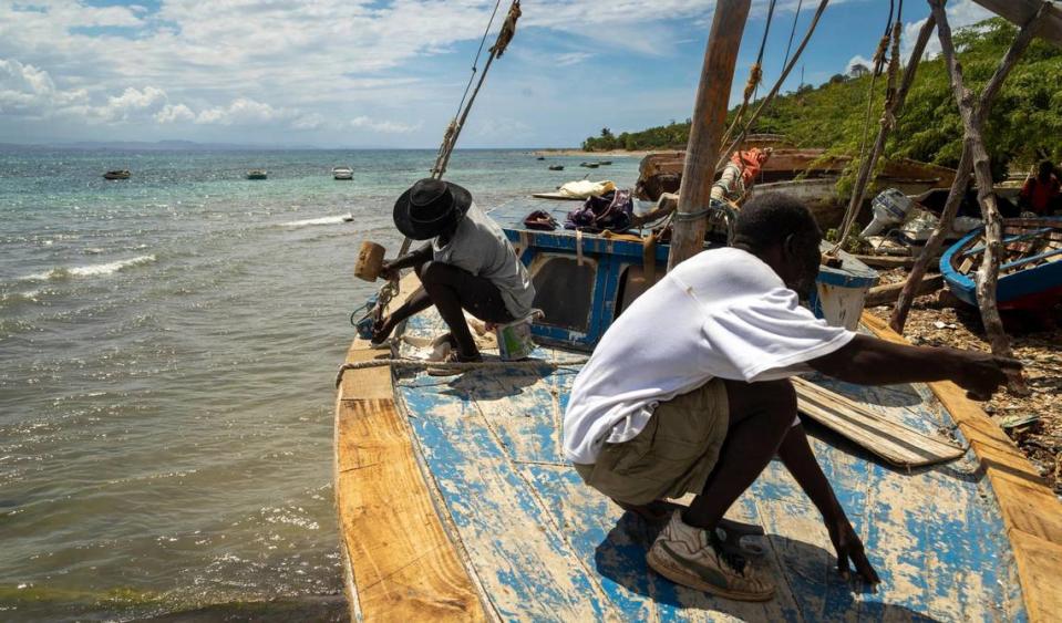 Two men repair a boat on March 26, 2022, on a beach in Île de la Tortue, off mainland Haiti along the northwest coast. The island’s seaports are helping spawn a human tide in migration for those lacking legal channels to leave Haiti.