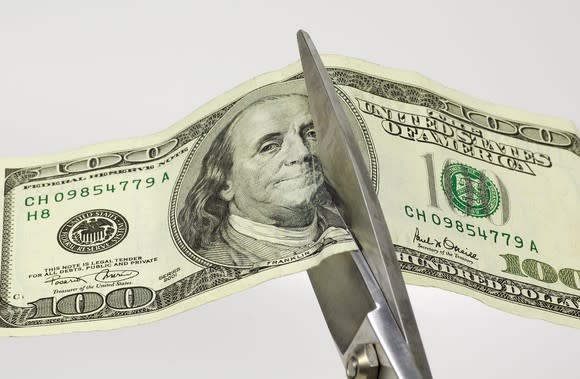 Scissors cutting a hundred-dollar bill in half.