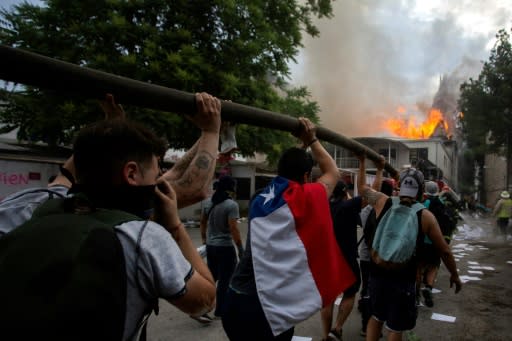 Demonstrators hold up a hose as flames engulf the Pedro de Valdivia University following a protest against the government of Chilean President Sebastian Pinera in Santiago, on November 8, 2019.Unrest began in Chile last October 18 with protests against a rise in transport tickets and other austerity measures that descended into vandalism, looting, and clashes between demonstrators and police