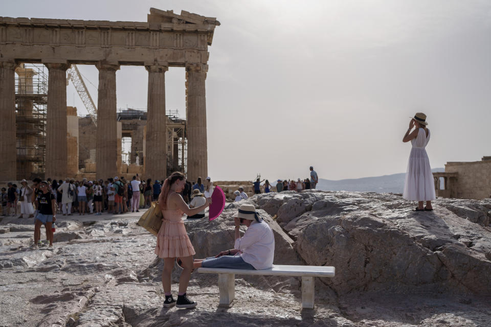 A tourist uses a hand fan to cool down another one sitting on a bench in front of the Parthenon at the ancient Acropolis, in Athens, Wednesday, June 12, 2024. The ancient site was closed to the public for five hours due to a heat wave that pushed temperatures to 39 degrees Celsius (102 Fahrenheit) in the capital and even higher in parts of central Greece. (AP Photo/Petros Giannakouris)