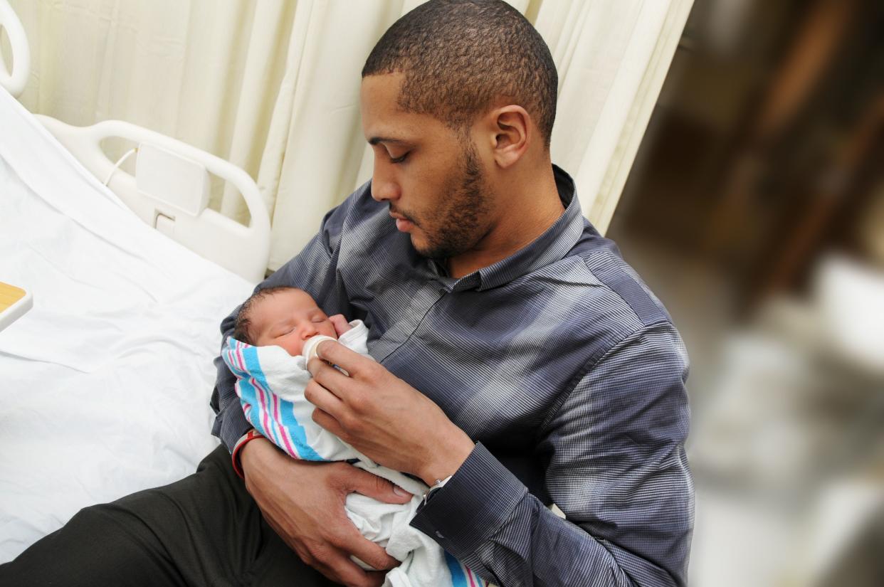 African American man sitting holding and feeding newborn infant child in his arms
