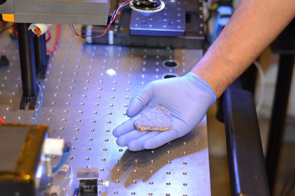 Rohit Bhartia of NASA's Mars 2020 mission holds a slice of a meteorite scientists have determined came from Mars. This slice will likely be used here on Earth for testing a laser instrument for NASA's Mars 2020 rover; a separate slice will go to Mars on the rover. <cite>NASA/JPL-Caltech</cite>