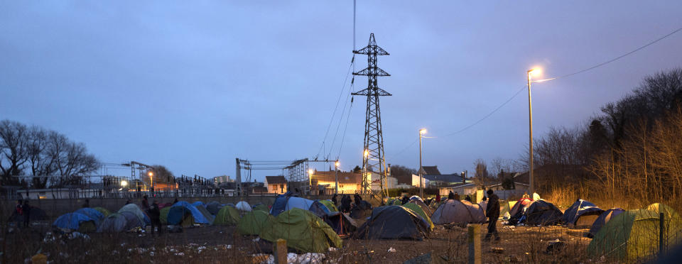 In this photo taken on Wednesday Jan. 16, 2019 A migrant walks through tents in a makeshift camp in Calais, northern France. Border control officers patrolling the land, sea and air of northern France are combing beaches, dunes and the frigid, murky coastal waters in a bid to end a high-risk but growing tactic by a group of mostly Iranian migrants desperate to get to Britain: sneaking across the English Channel in rubber boats. (AP Photo/Michel Spingler)