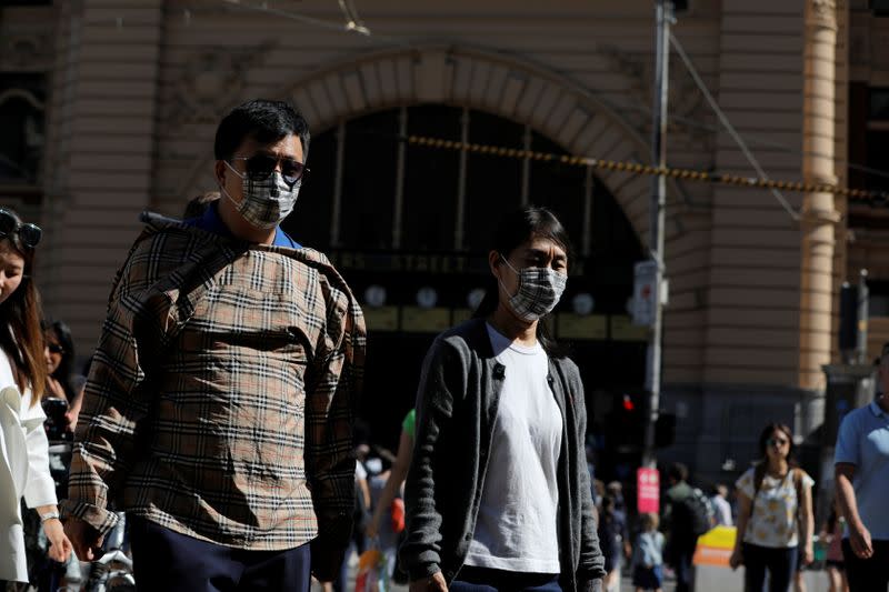People wearing face masks walk by Flinders Street Station after cases of the coronavirus were confirmed in Melbourne