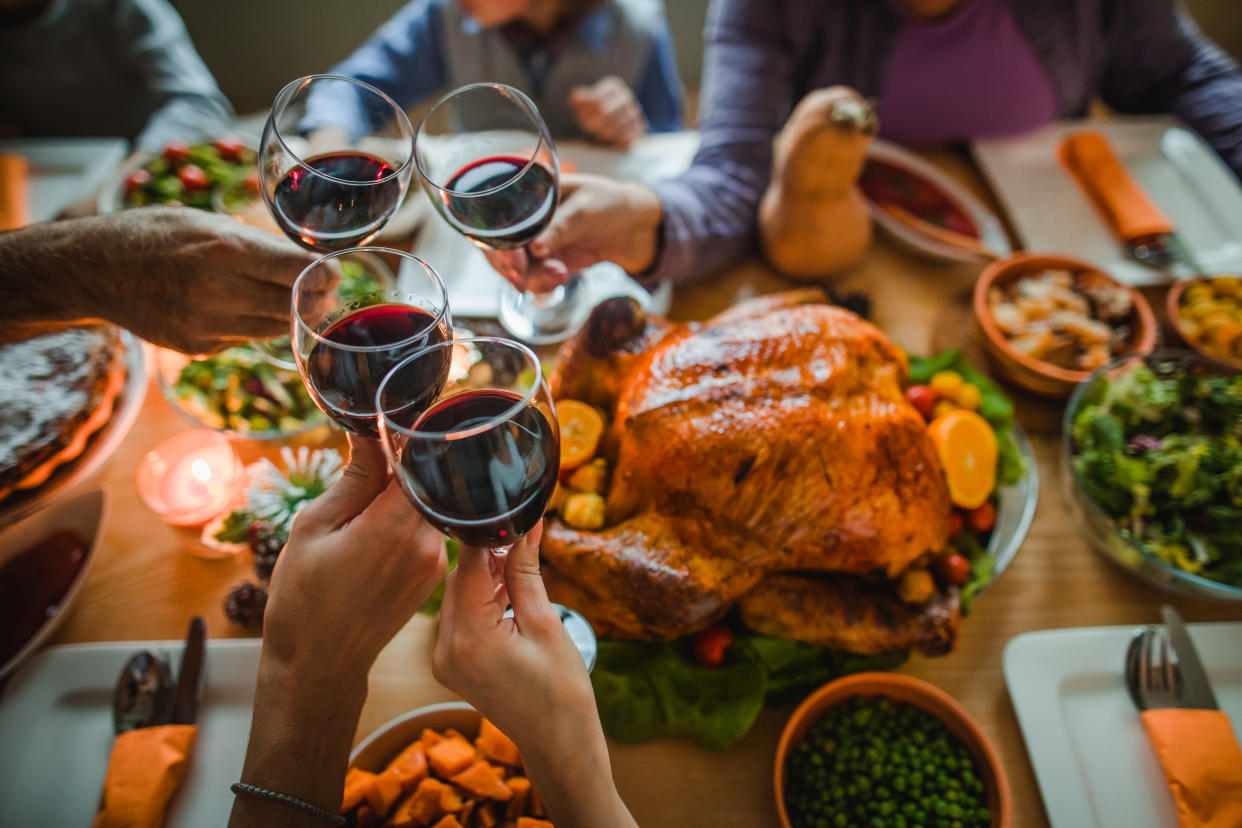 Group of unrecognizable people toasting with wine during Thanksgiving dinner at dining table.