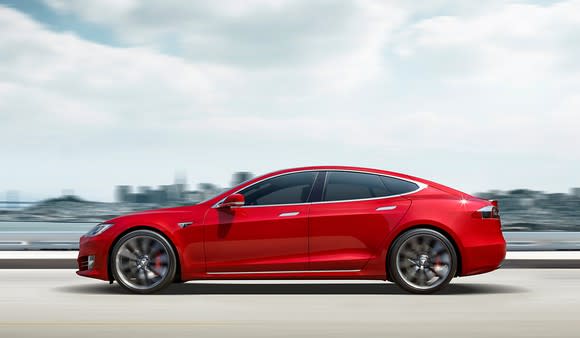 A red Tesla Model S luxury sedan driving down a road.