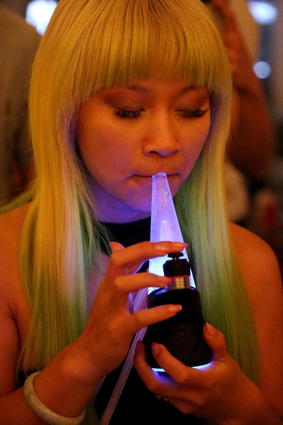 A person inhales from a conical, purple-lit concentrate vaporizer