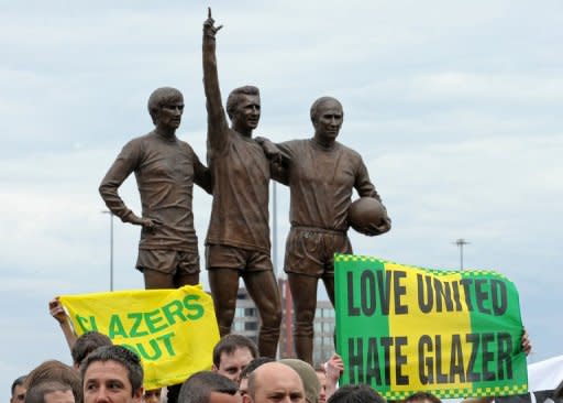 Hinchas del Manchester United se manifiestan contra el ingreso del club a la Bolsa de Valores de Nueva York, frente a una estatua con las figuras de George Best, Dennis Law y Bobby Charlton, el 09 de agosto de 2012 en Manchester. (AFP | andrew yates)