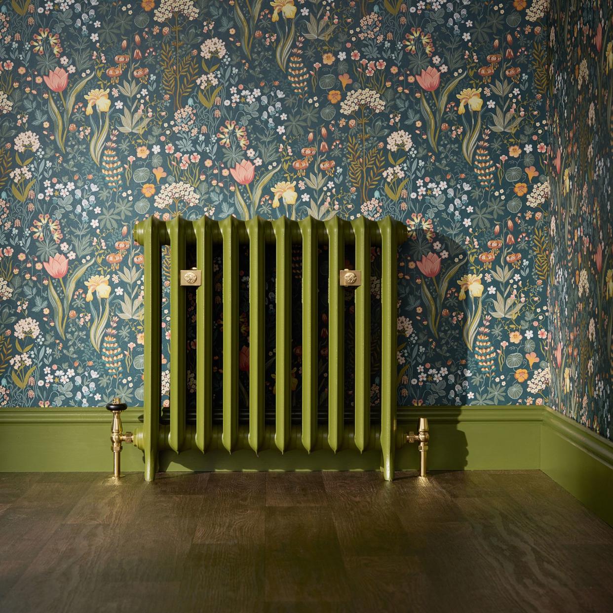  Heating systems green radiator with painted skirting board and floral decorative wallpaper. 