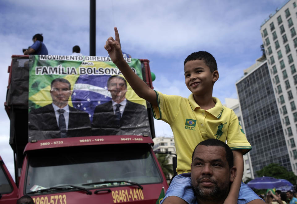 A man and youth attend a rally in favor of Brazil's President Jair Bolsonaro, in front of a photo of Jair with his son Flavio, on Copacabana beach in Rio de Janeiro, Brazil, Sunday, May 26, 2019. The pro-Bolsonaro rally follows anti-government protests against cuts in the education budget as the president also battles an uncooperative Congress, a family corruption scandal and falling approval ratings after five months in office. (AP Photo/Silvia Izquierdo)