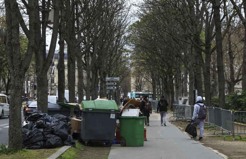 FILE - People walk past uncollected garbage in Paris, March 20, 2023 as strikes continue with uncollected garbage piling higher by the day. (AP Photo/Aurelien Morissard, File)