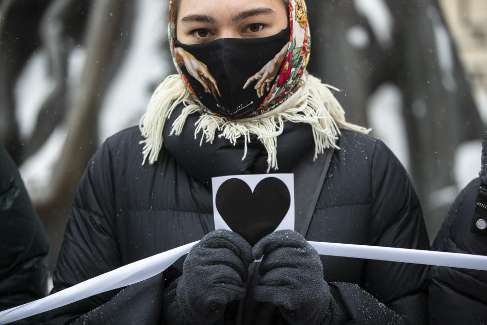 A woman holds an image of heart and a white ribbon as she stands in a line of women during a rally in support of jailed opposition leader Alexei Navalny and his wife Yulia Navalnaya at Arbat street in Moscow, Russia, Sunday, Feb. 14, 2021. (AP Photo/Pavel Golovkin)