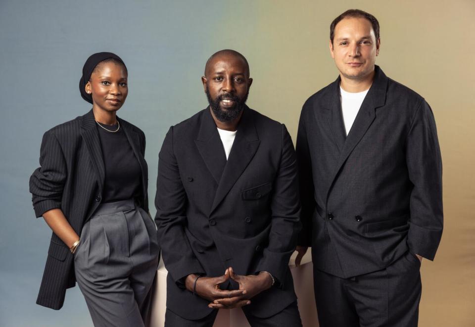 Anta Diaw, Ladj Ly and Alexis Manenti smile and pose together in dark outfits in front of a cube.