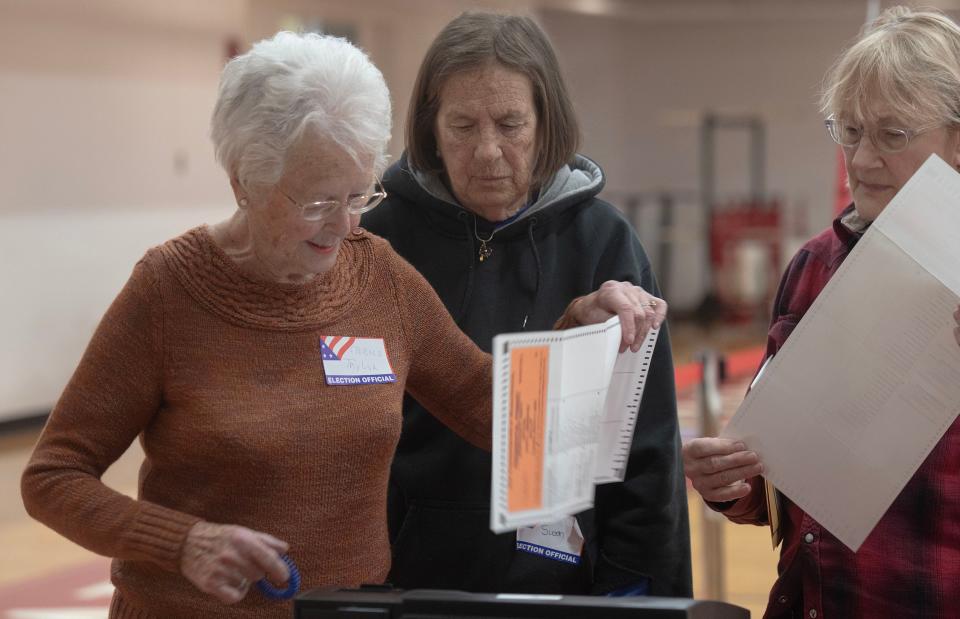 Poll workers Carol Taylor, left, Susan Ridenour and Vicki Marchant, right, coax folded mail-in ballots into the voting machine at the Hyannis Youth and Community Center where three town of Barnstable precincts voted in Tuesday's primary.