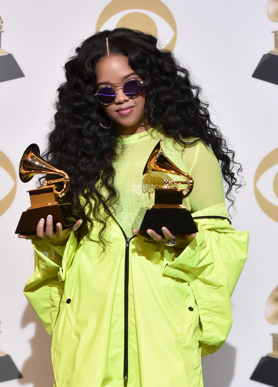 H.E.R. wearing a lime green outfit while holding two Grammys