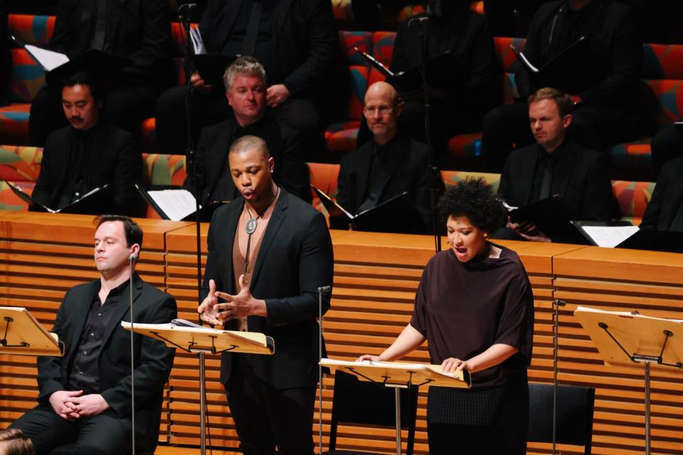 Singers at music stands, with a seated chorus behind them.