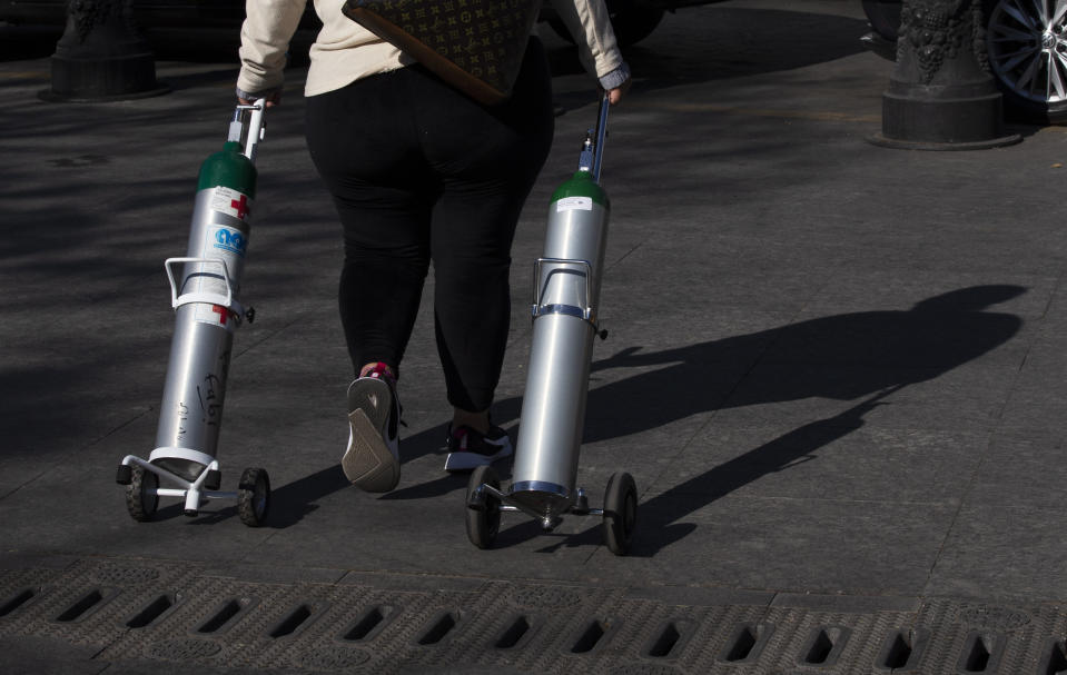 A woman walks off after refilling two tanks with oxygen for patients with COVID-19 in the Iztapalapa district of Mexico City, Tuesday, Jan. 26, 2021. The city is offering free oxygen refills for patients with COVID-19. (AP Photo/Marco Ugarte)