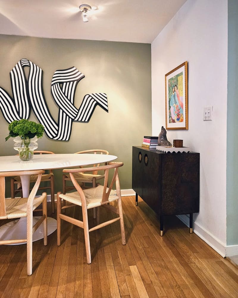 Dining room with one gray accent wall with statement art piece, oval white table with wood and rattan chairs