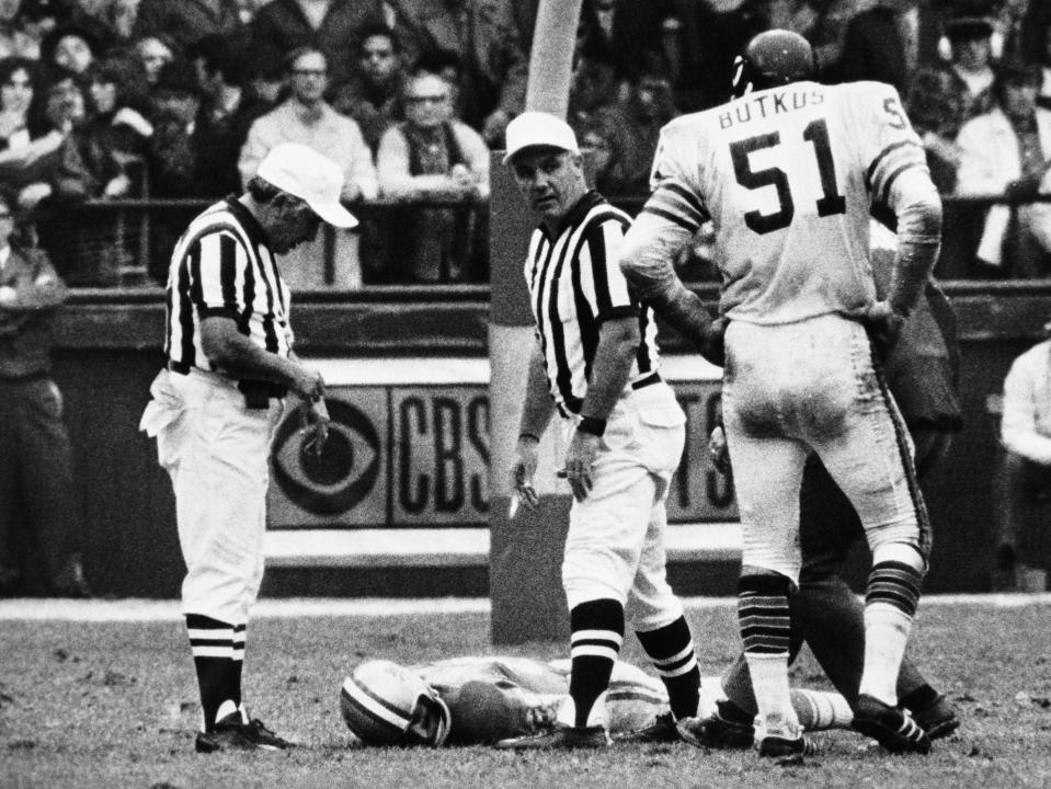 Chuck hughes lies on the field face down as two referees watch in a black in white picture.