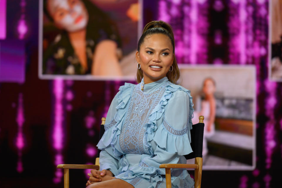 Chrissy Teigen is photographed while sitting in a chair on a set