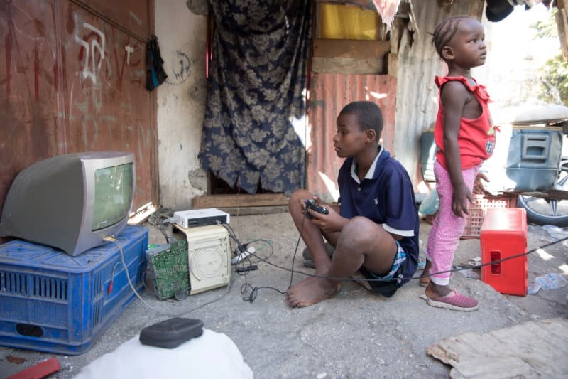 Boy plays video games on the street, outside of Notre Dame de l'Assomption Cathedral (Our Lady of the Assumption), in Port-au-Prince