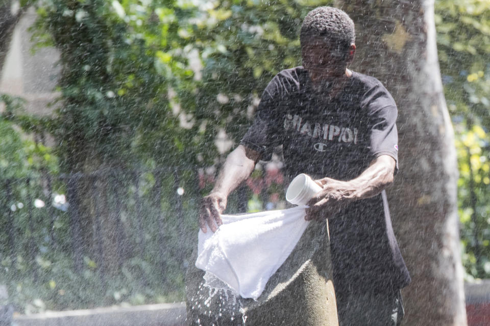 A man uses a park sprinkler to cool off, Wednesday, Aug. 29, 2018, in New York. Dangerously high heat in the Northeastern United States has prompted emergency measures including extra breaks for players wilting at the U.S. Open tennis tournament. (AP Photo/Mary Altaffer)